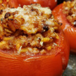 A close-up image of stuffed tomatoes, brimming with meat, veggies, and rice, topped with melted mozzarella and garnished with fresh basil