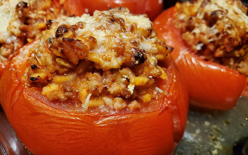 A close-up image of stuffed tomatoes, brimming with meat, veggies, and rice, topped with melted mozzarella and garnished with fresh basil