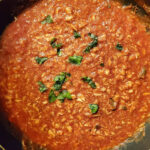 Bowl of Pasta al Tonno topped with tomato sauce, fresh tuna, and fresh herbs.