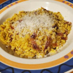 A delicious-looking Saffron Risotto with Speck, plated and ready to eat. The risotto is golden brown and creamy, and the speck is smoky and flavorful, featured on Authentic Italian Recipes website.