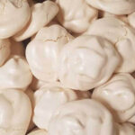 A batch of pristine white Italian Meringue cookies plated on a contrasting light brown dish, showcasing their crispy lightweight texture.