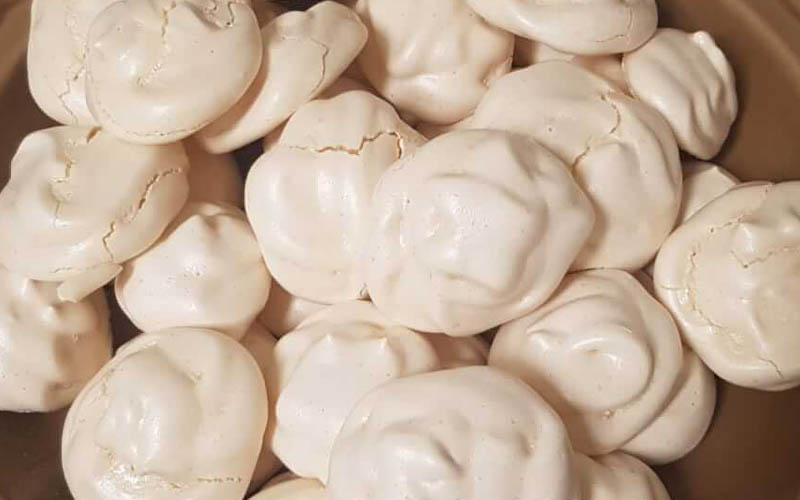 A batch of pristine white Italian Meringue cookies plated on a contrasting light brown dish, showcasing their crispy lightweight texture.