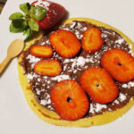 A plate of Sweet Crespelle, thin Italian pancakes topped with Nutella and fruit, on a rustic table setting.