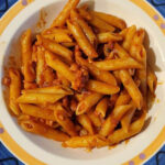 A bowl of Pasta all'Amatriciana with guanciale, tomato sauce, topped with Parmesan and olive oil.