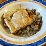 A delicious-looking Turkey and Vegetable pie plated in a shallow bowl. The pie is golden brown and flaky, and the vegetables are perfectly cooked. The pie is garnished with fresh parsley and a sprig of rosemary.